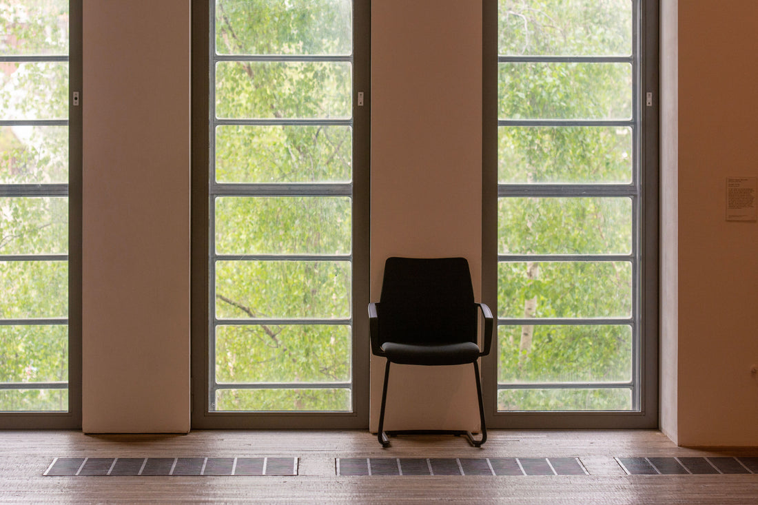 A single wooden chair in a bright empty room beside tall windows, morning light across the floor
