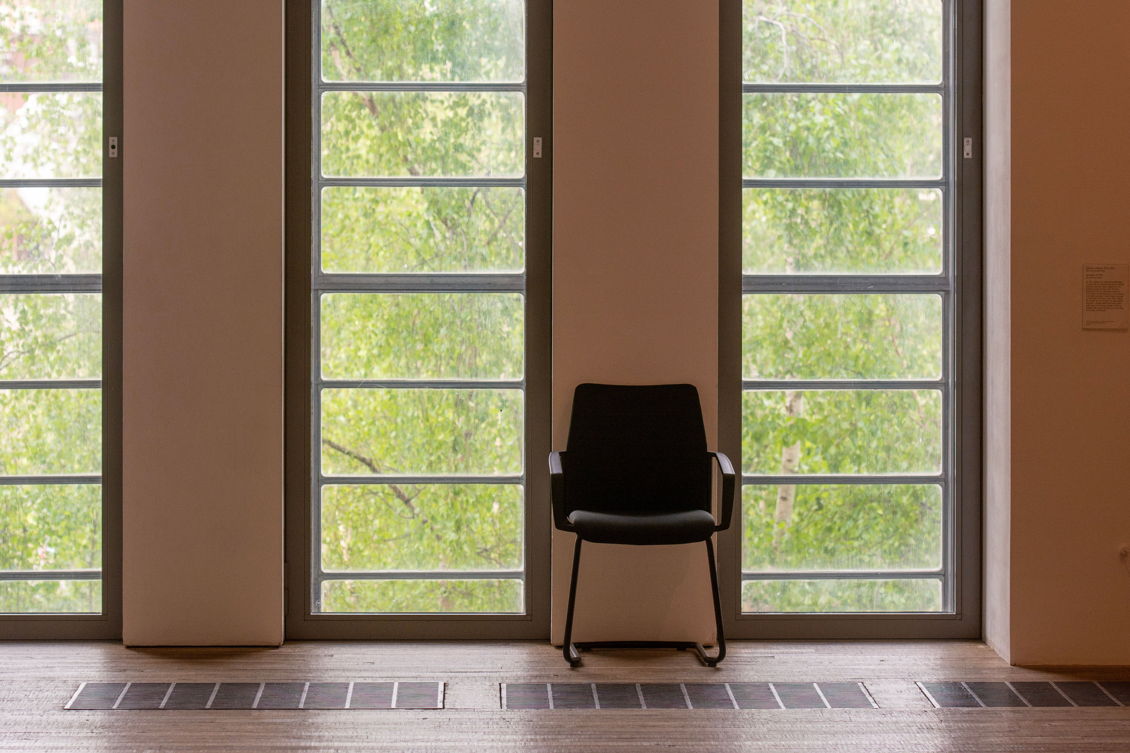 A single wooden chair in a bright empty room beside tall windows, morning light across the floor